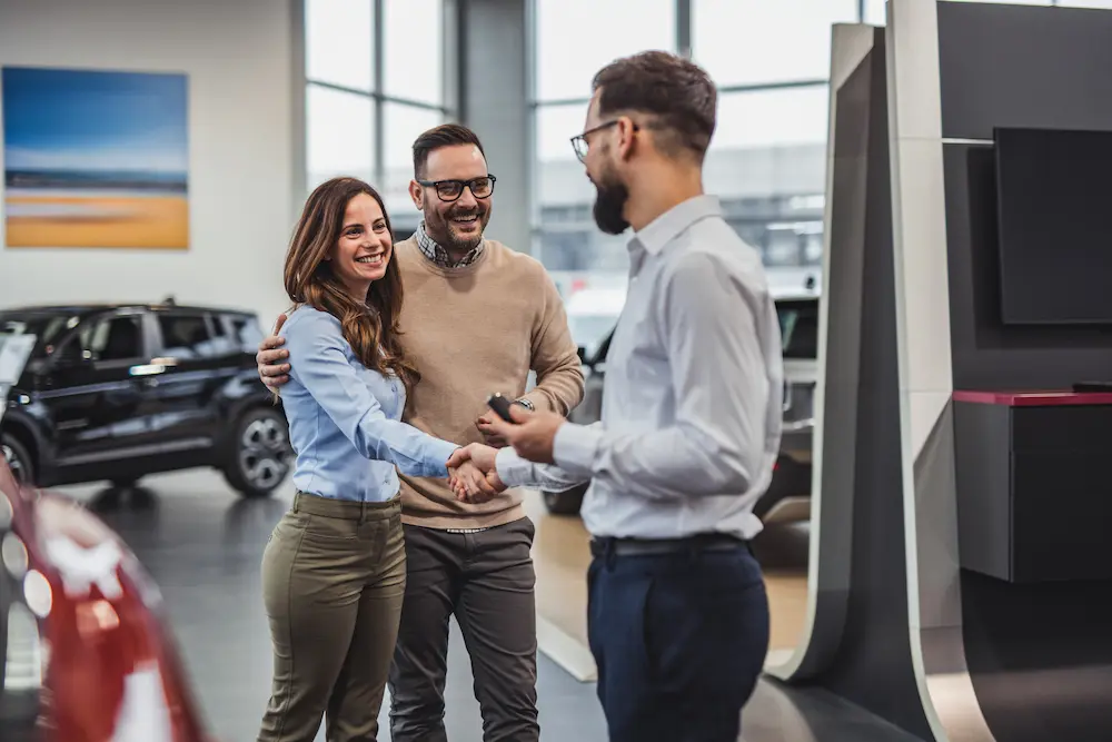 Happy couple receive keys to new car from salesperson